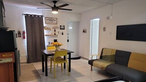 A compact living space with a dining area, a sofa, a ceiling fan, and a coffee bar sign. - Sunset Private Studio (Toa Baja)