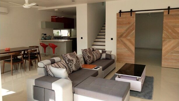 Een moderne woonkamer met een modulaire bank, een eettafel en stoelen. In de achtergrond is een keuken te zien met een trap naar een ander niveau.