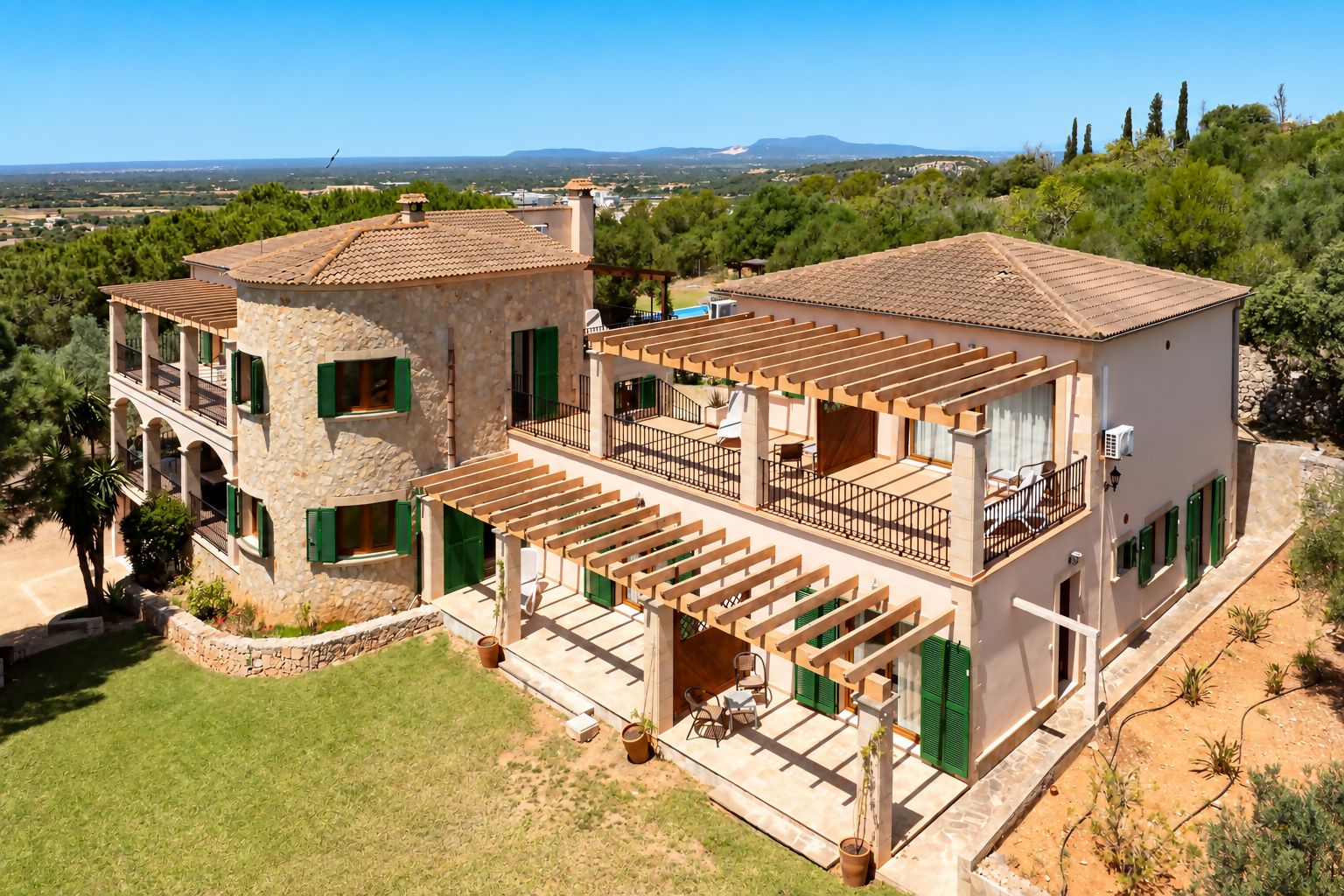 A two-story stone house with a balcony, a pool, and a view of the countryside.