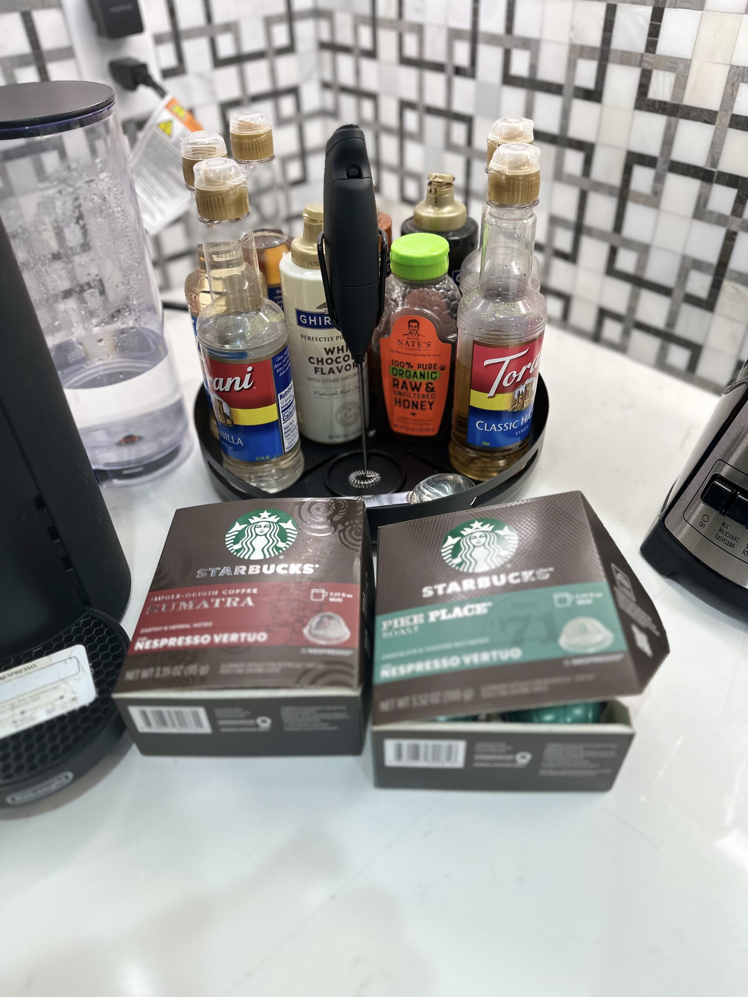 Eine Kaffeemaschine mit verschiedenen Kaffeekapseln und Flaschen mit Sirup und Honig.