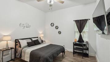 A bedroom with a bed, bedside tables, a desk, a chair, a ceiling fan, and a window with curtains.
