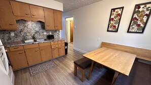 A compact kitchen with wooden cabinets, a granite countertop, and a dining area with a bench and table.