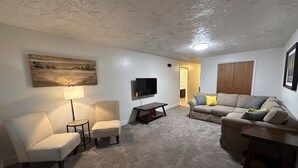 A living room with a sofa, chairs, a TV, and a painting on the wall.