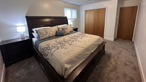A bedroom with a bed, nightstands, a wooden wardrobe, and a ceiling light fixture.