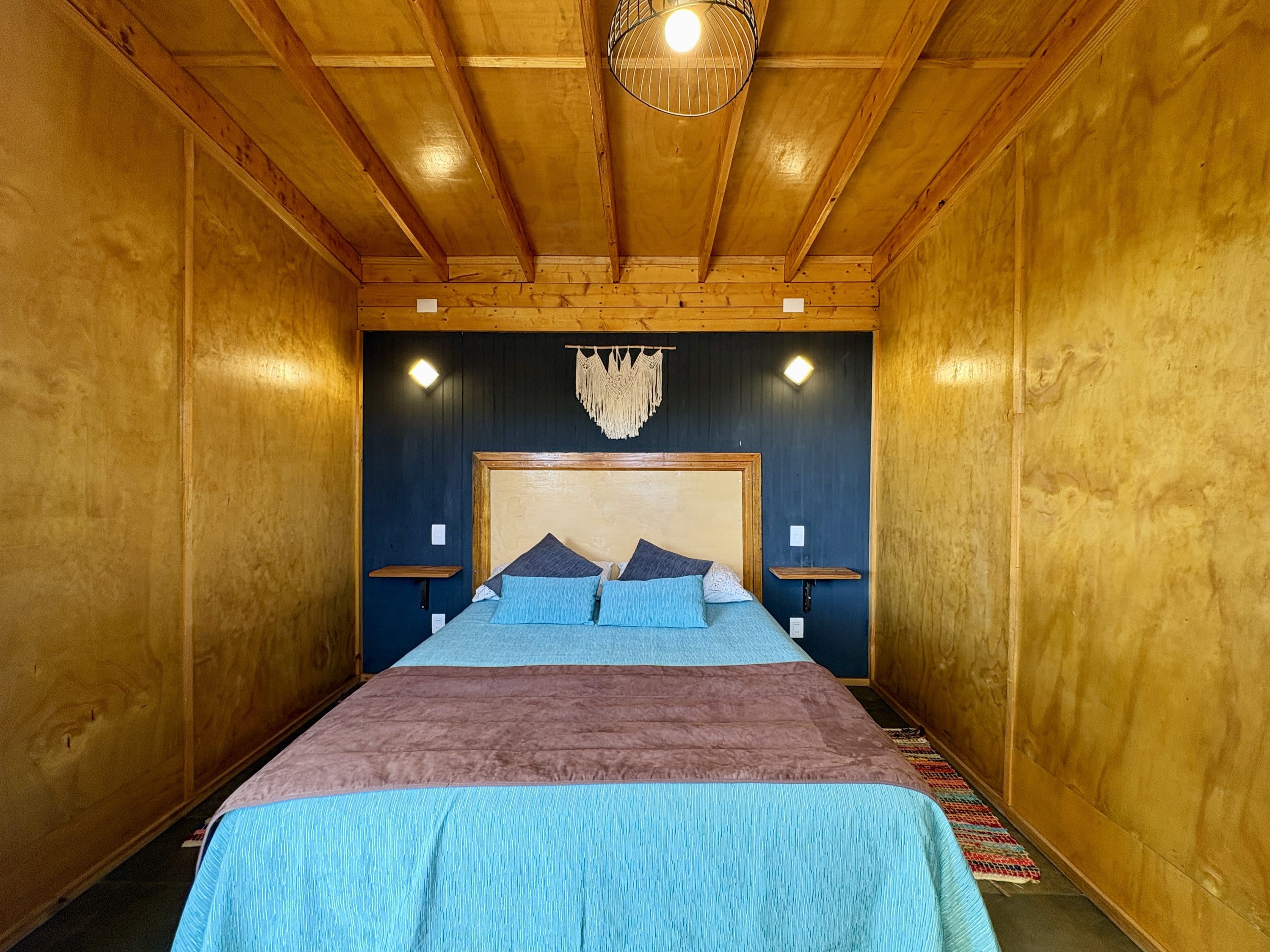 A wooden-paneled room with a bed, two bedside tables, and a hanging macrame light fixture.