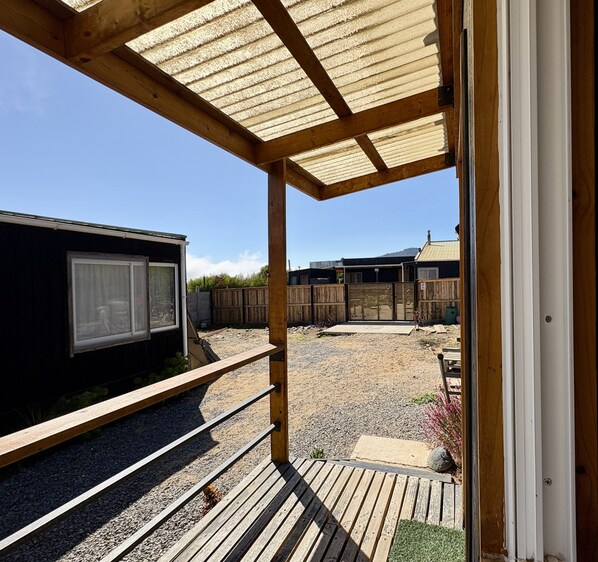 Una terraza de madera con una pérgola, un área de grava y un patio cercado.