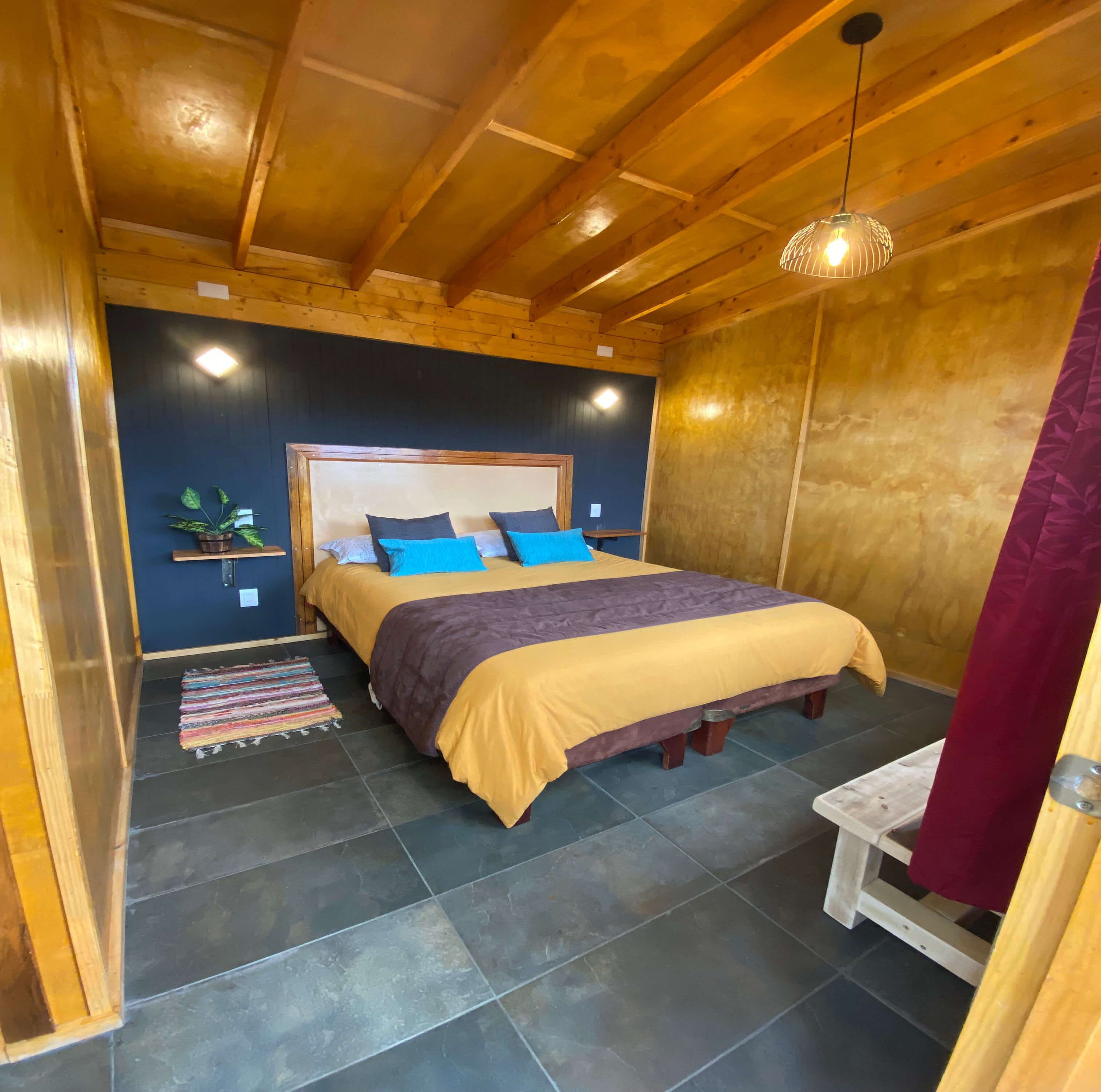 A wooden-paneled room with a bed, a small table, and a hanging light fixture.