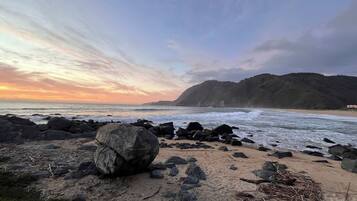 A beach with large rocks in the foreground and a hilly landscape in the background.