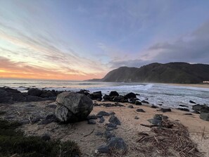 Una playa con rocas grandes al frente y un paisaje montañoso en el fondo.