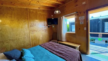 A wooden cabin room with a bed, a bench, a television, and a window with a view of the outside.