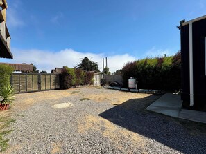 Un patio con grava, una valla, un tanque blanco y un edificio al fondo.