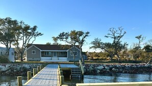 A wooden pier leading to a house by a body of water, with a bench at the end. - Core Sound beauty! Easy access to Core Banks and Cape Lookout. - SLEEPS 11 (Davis)