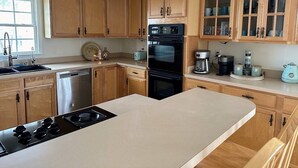 A kitchen with wooden cabinets, a stainless steel dishwasher, a black oven, and a countertop with a coffee maker and other appliances. - Core Sound beauty! Easy access to Core Banks and Cape Lookout. - SLEEPS 11 (Davis)