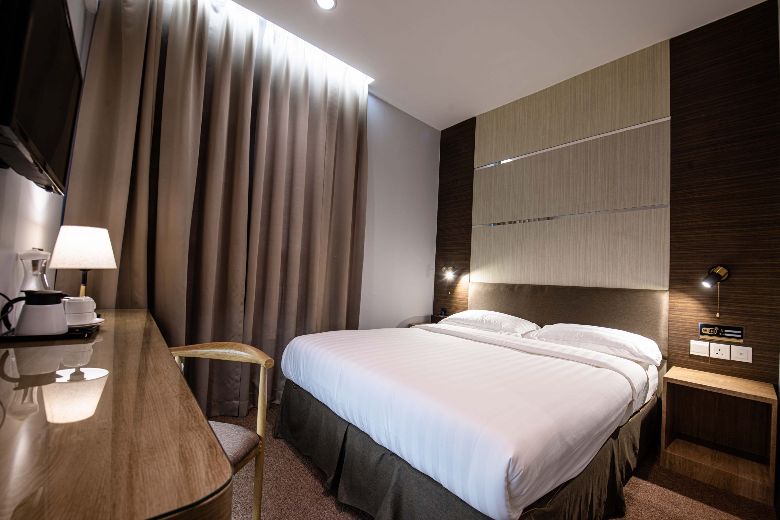 Una habitación de hotel moderna con una cama grande, un escritorio con lámpara, una silla y una mesita de noche con lámpara.