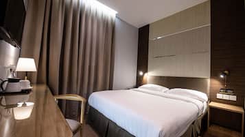Una habitación de hotel moderna con una cama grande, un escritorio con lámpara, una silla y una mesita de noche con lámpara.