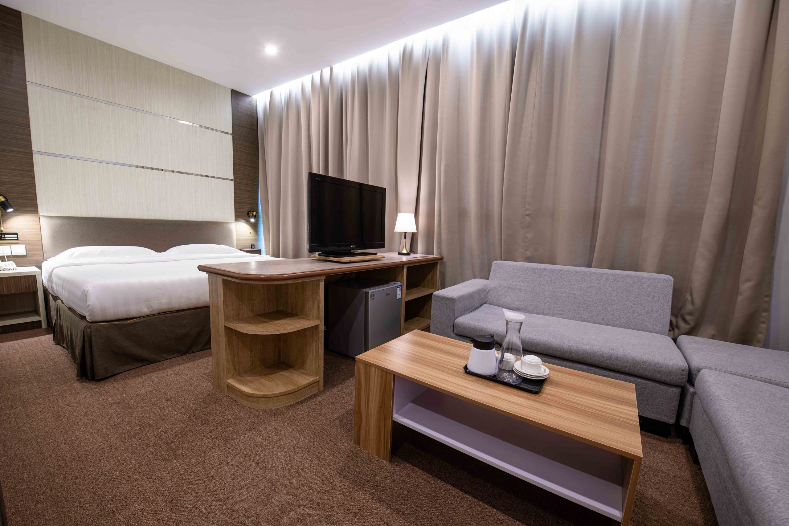 A hotel room with a bed, a desk with a television, a sofa, and a coffee table.