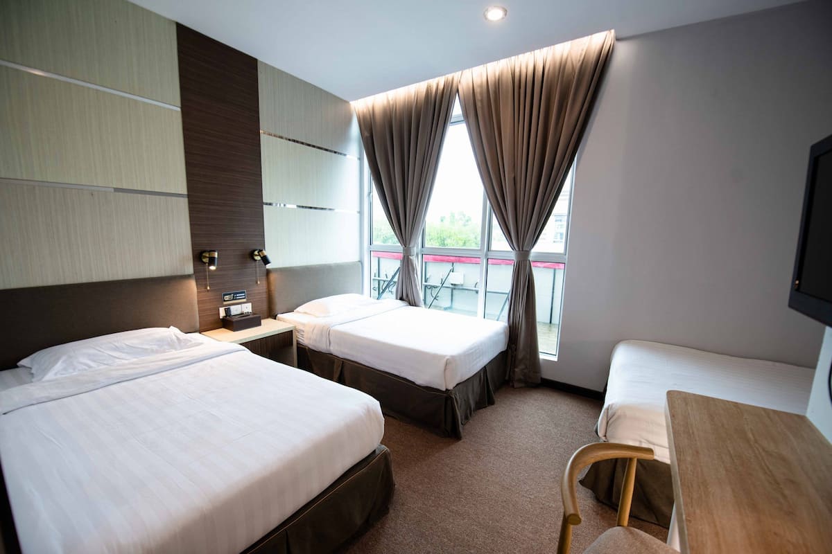 Habitación de hotel con dos camas, un escritorio y una silla. Cuenta con una ventana con cortinas, un televisor de pantalla plana montado en la pared y una mesita de noche con lámpara.