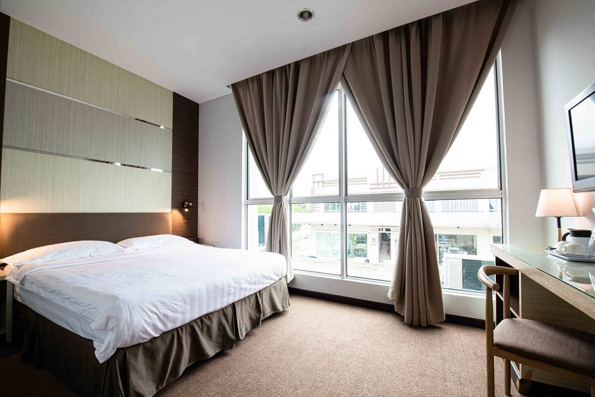 Una habitación de hotel con cama, escritorio y ventana con cortinas.