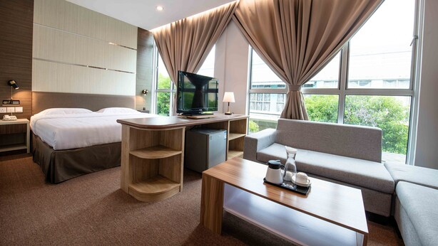 A modern hotel room with a bed, a desk, a sofa, and a television. - Hotel Meliden (Sandakan)