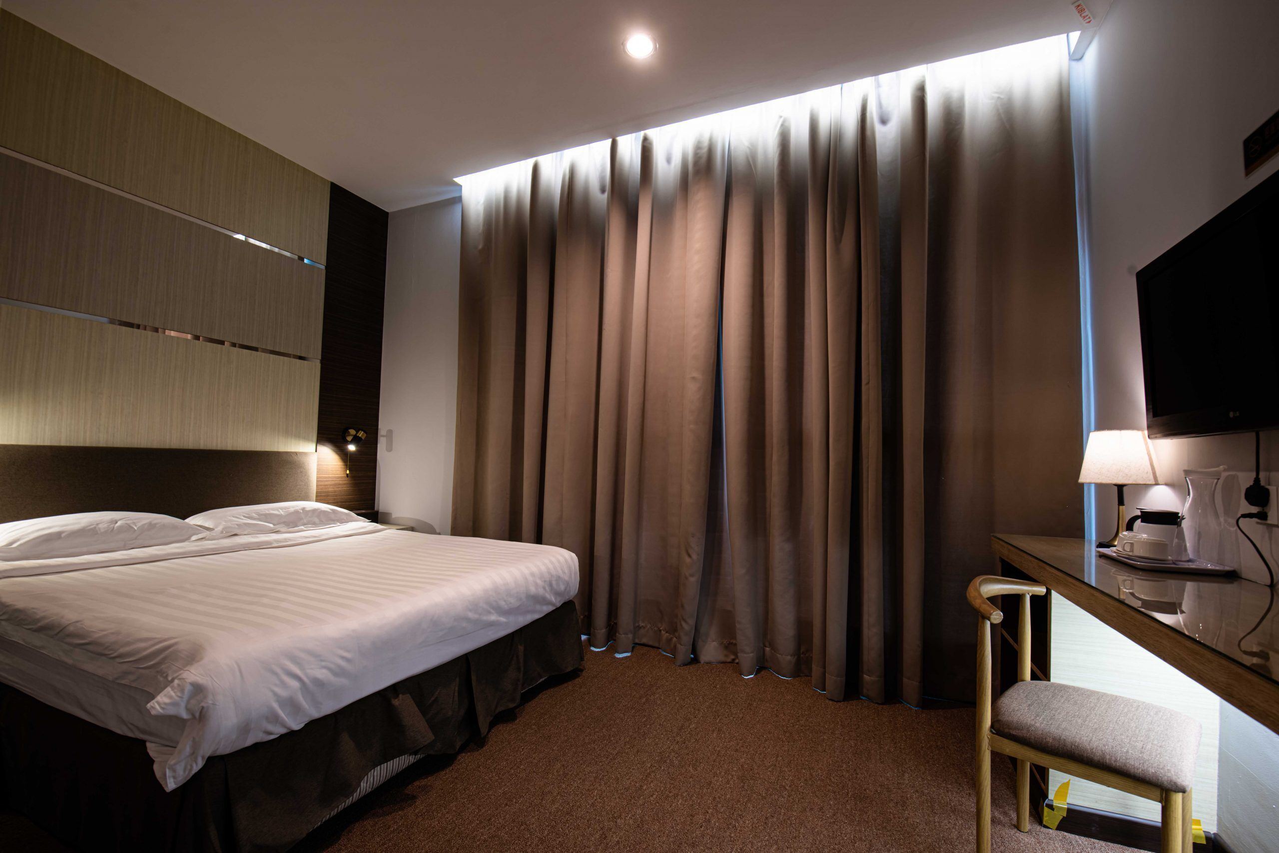 Une chambre d’hôtel avec un lit, un bureau et une chaise, une télévision et des rideaux.