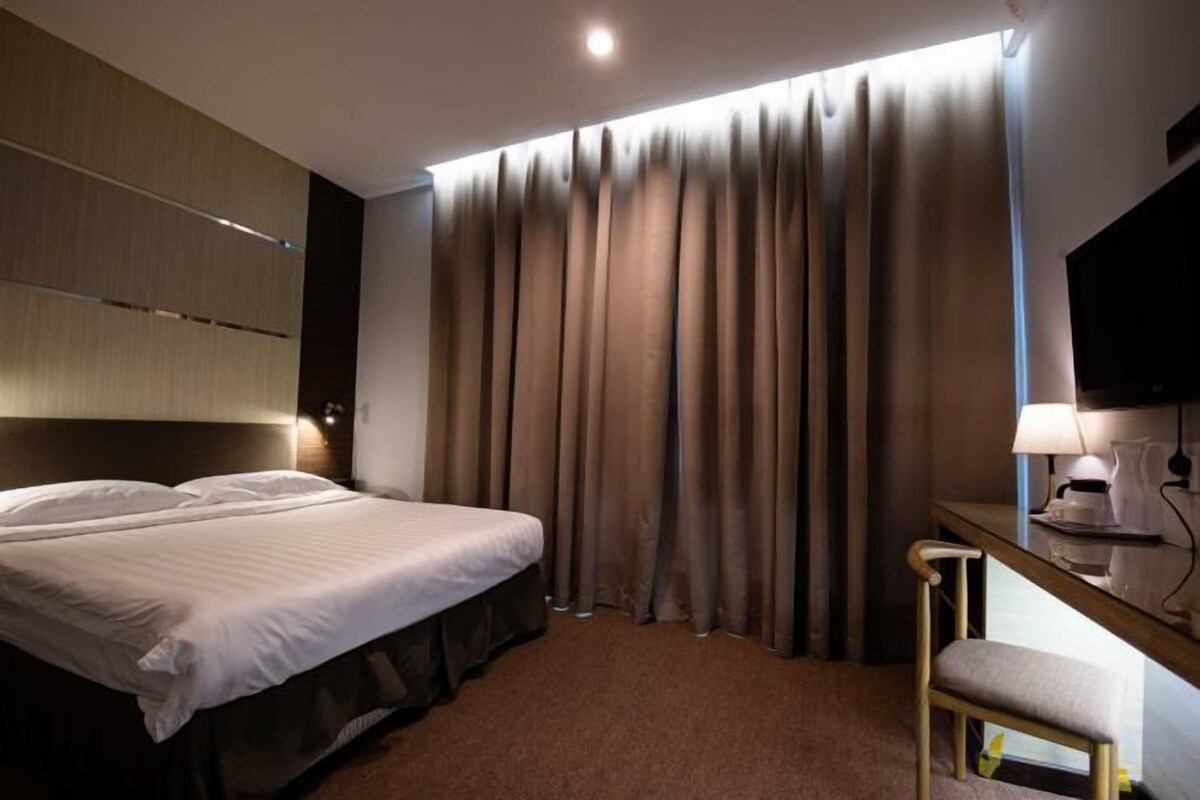A hotel room with a bed, a desk, a chair, and a large window with curtains.