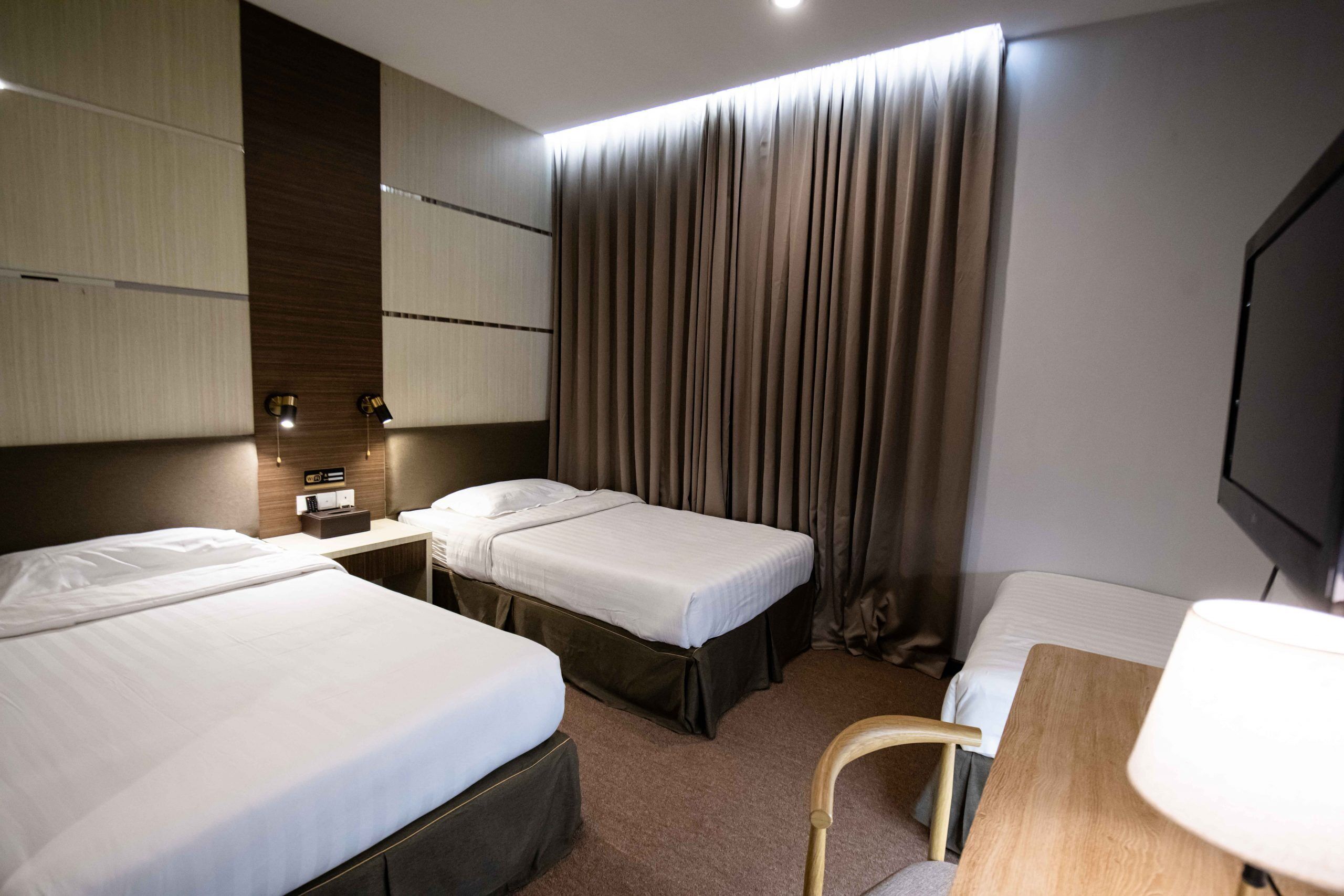 Une chambre d’hôtel avec deux lits, un bureau, une chaise, une télévision et un rideau.