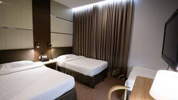 A hotel room with two beds, a desk, a chair, a TV, and a curtain.