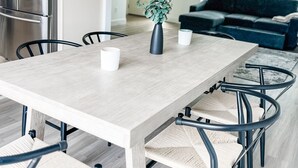Et moderne køkken med en stor ø, rustfrie stålapparater og et spiseområde med et lyst træbord og metalstole.