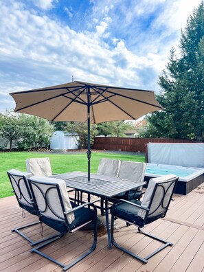 An outdoor patio with a table and chairs, a large umbrella, and a hot tub.