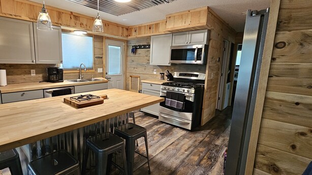 A compact kitchen with wooden cabinets, a central island, stainless steel appliances, and bar stools.