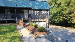 A two-story house with a porch, a small garden, and a gravel driveway.