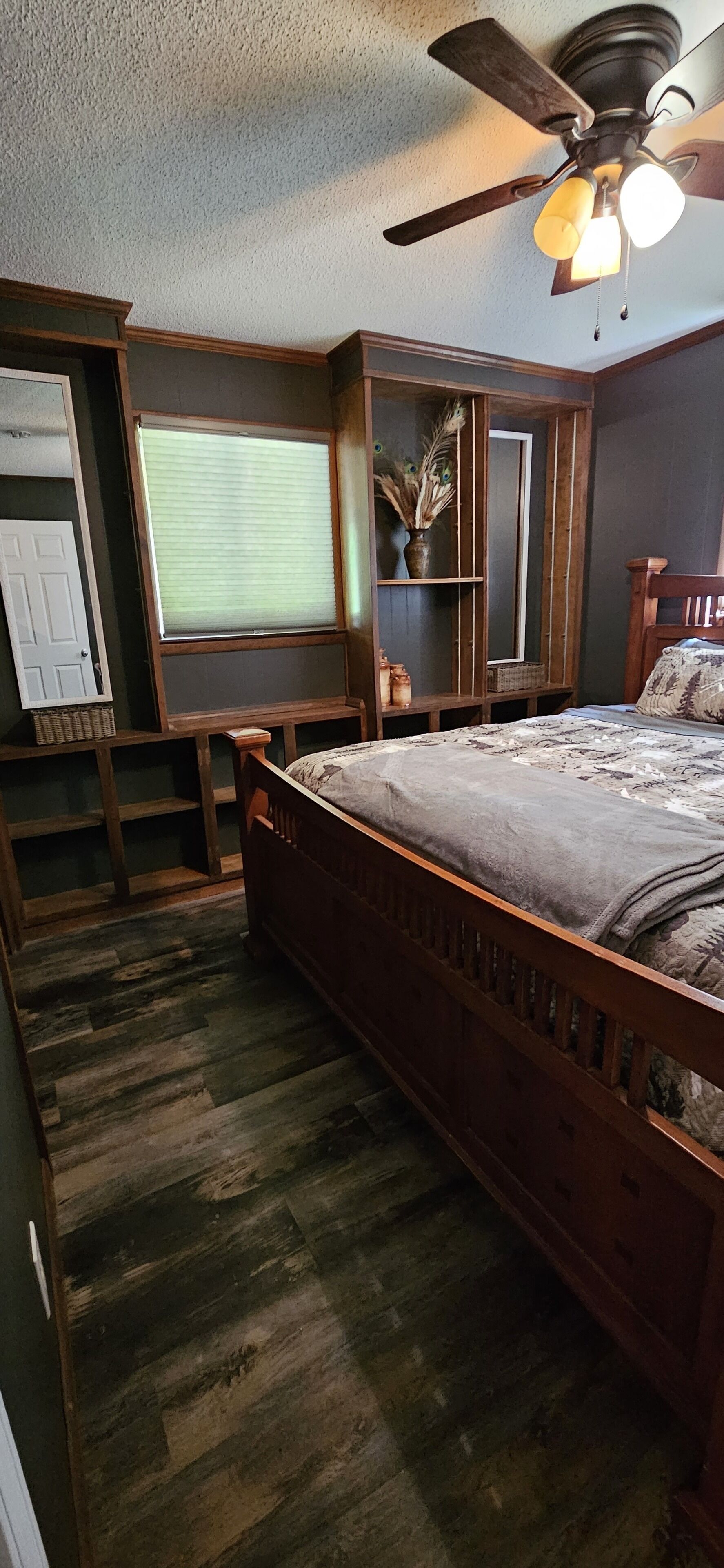A bedroom with a wooden bed, a ceiling fan, a window with blinds, and a wooden wardrobe.