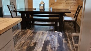 A kitchen with wooden walls, a dining table, chairs, a ceiling fan, and a refrigerator.