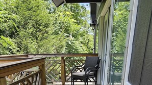 A wooden deck with a railing, a bench, and a window overlooking a forested area.