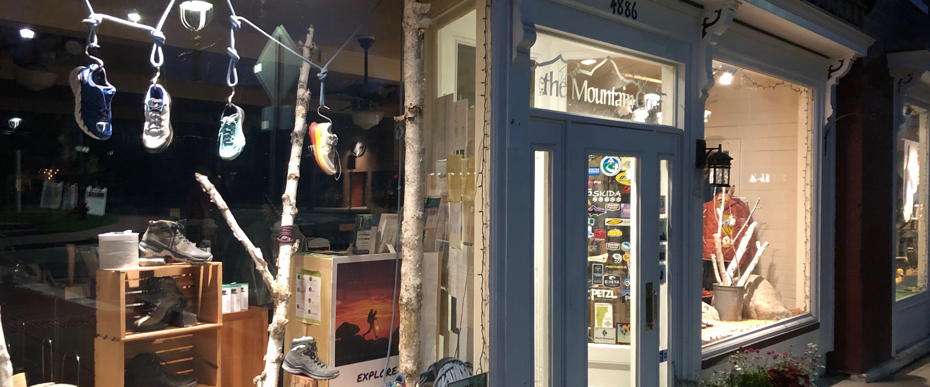 En butik med en blå dörr, olika typer av skoutställningar och en skylt med texten ”The Mountain Co.”.