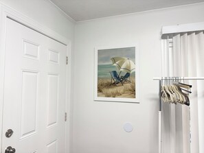 A room with a white door, a framed beach scene painting, and a clothing rack. - Modern Coastal Villa w Luxury Swim Spa & Art (Sarasota)