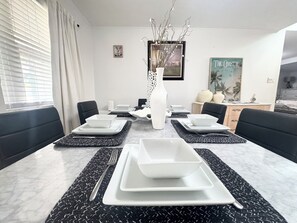 Een eetruimte met een tafel gedekt voor vier personen, zwarte stoelen met kussens en een witte vaas als middelpunt.