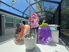 Een ruimte met glazen wanden, een biljart, een grote decoratieve plant en een kleurrijke opblaasdecoratie.