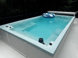Una bañera de hidromasaje rectangular con un aro inflable azul y blanco, rodeada por una terraza blanca.