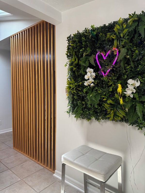 Ein Raum mit einer Trennwand aus Holzleisten, einer weißen Bank und einer an der Wand befestigten Zimmerpflanze mit einem Neonherz.