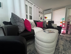 A living room with a sofa, ottoman, and a bookshelf.