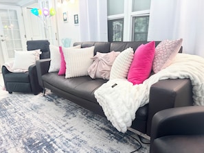 Un soggiorno con un divano marrone scuro, numerosi cuscini di vari colori, una coperta soffice bianca e un tappeto decorato.