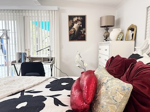 Een slaapkamer met een bed, een bureau, een stoel, een dressoir en een raam met jaloezieën.