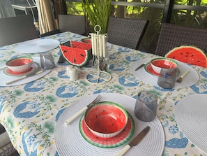 A table set with plates, bowls, and cutlery, featuring a watermelon pattern on the tablecloth.