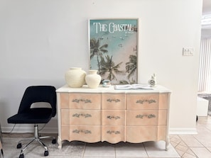 Een kamer met een witte kapstok, een zwarte stoel en een poster van een strandgezicht.