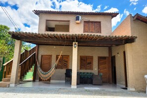 Una casa de dos pisos con un porche cubierto, una hamaca y fachada de ladrillo.