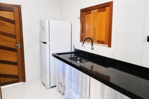 Una cocina con un refrigerador blanco, una encimera negra, un armario de madera y un fregadero.