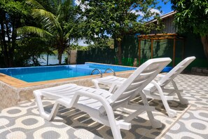 Une piscine avec des chaises longues et une terrasse carrelée.