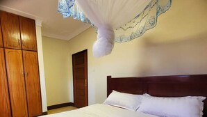 Una cama bien hecha con ropa blanca y un cabecero de madera en una habitación que tiene un armario de madera y una puerta.