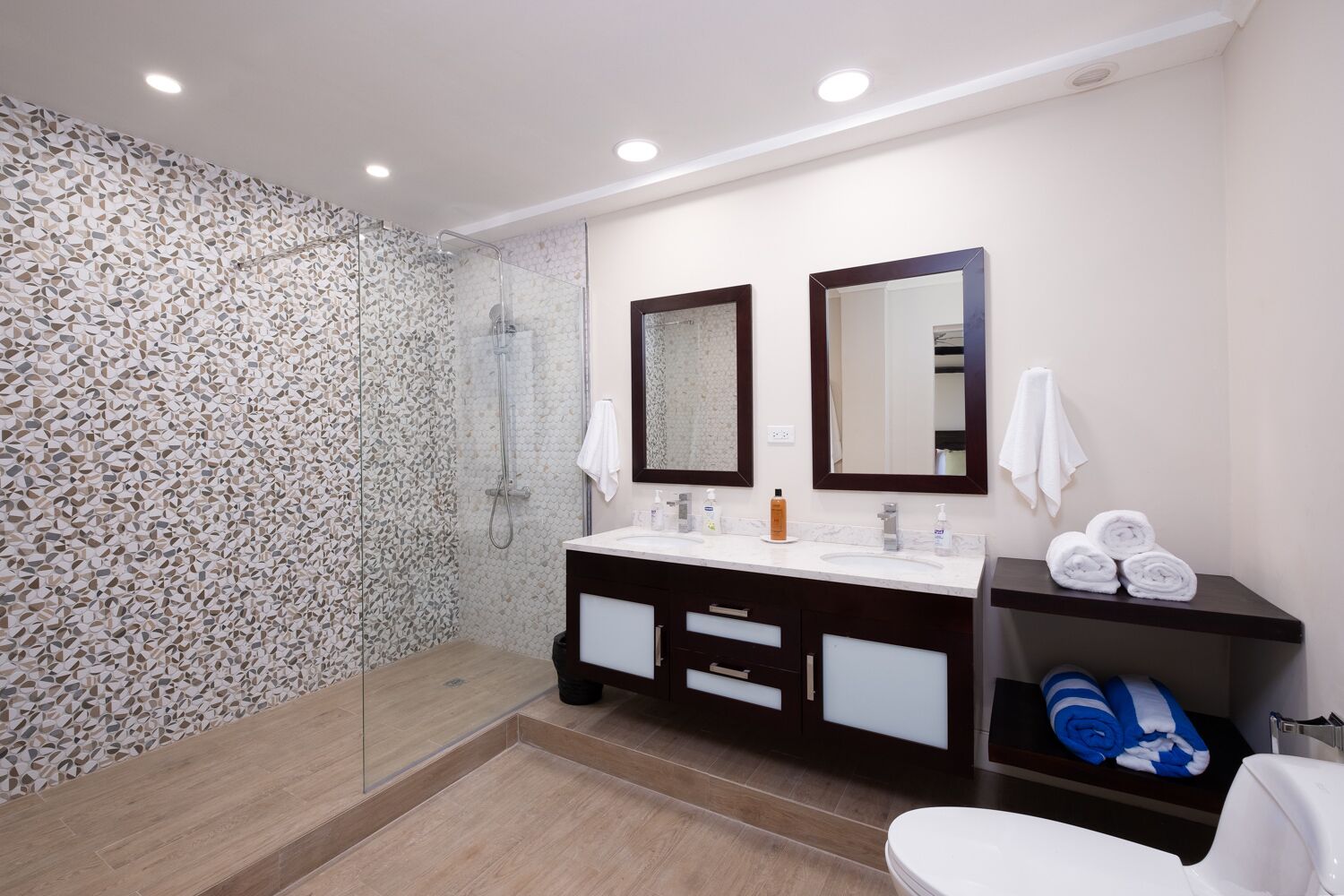 A modern bathroom with a shower, two sinks, and a toilet.